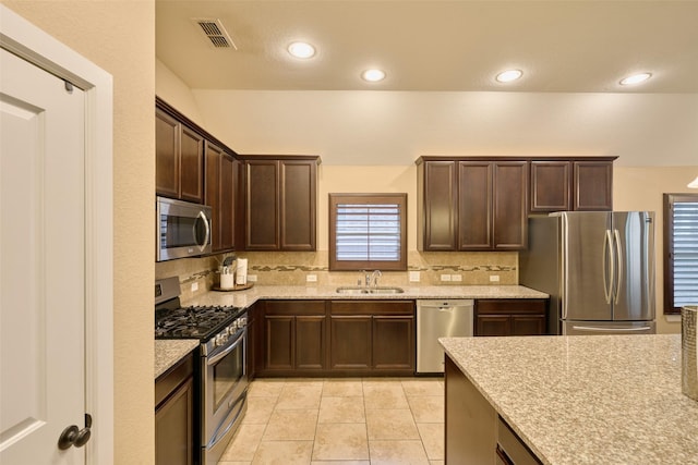 kitchen featuring sink, decorative backsplash, light tile patterned floors, light stone counters, and stainless steel appliances