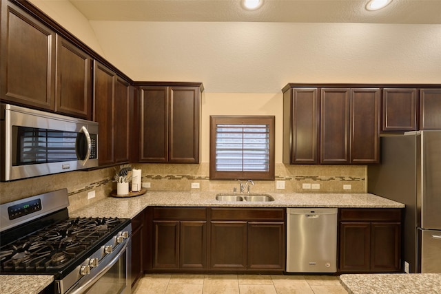 kitchen featuring appliances with stainless steel finishes, sink, decorative backsplash, light stone counters, and dark brown cabinets