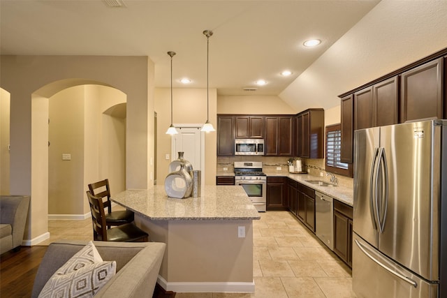 kitchen with sink, decorative light fixtures, a center island, stainless steel appliances, and light stone countertops