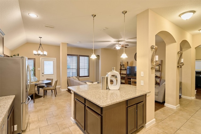 kitchen with light stone counters, decorative light fixtures, vaulted ceiling, stainless steel fridge, and ceiling fan with notable chandelier
