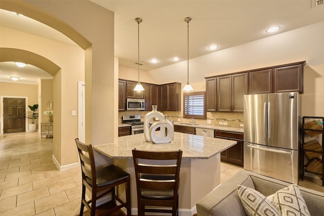 kitchen featuring a kitchen island, appliances with stainless steel finishes, decorative backsplash, hanging light fixtures, and light stone counters