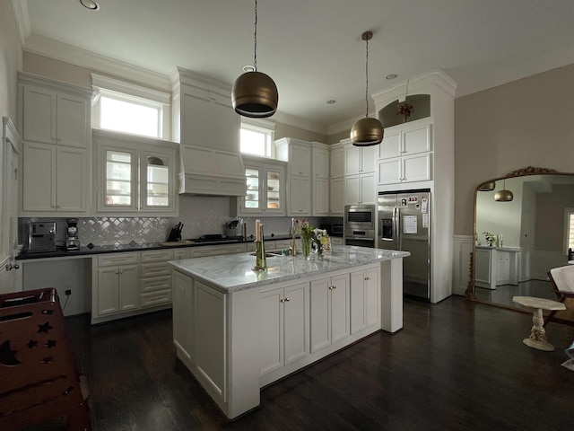 kitchen with white cabinetry, a kitchen island with sink, stainless steel appliances, light stone countertops, and decorative light fixtures