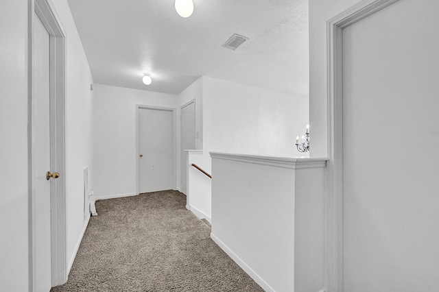 hall with carpet, visible vents, baseboards, and an upstairs landing