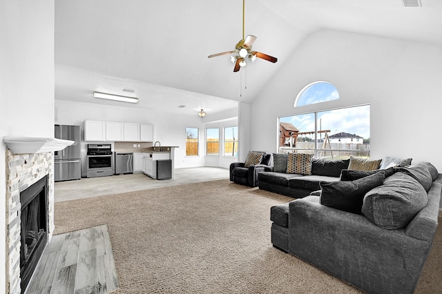 living room with visible vents, ceiling fan, light wood-style floors, a fireplace, and high vaulted ceiling