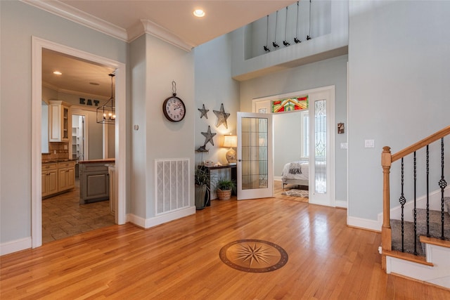 foyer entrance with an inviting chandelier, ornamental molding, and light hardwood / wood-style flooring