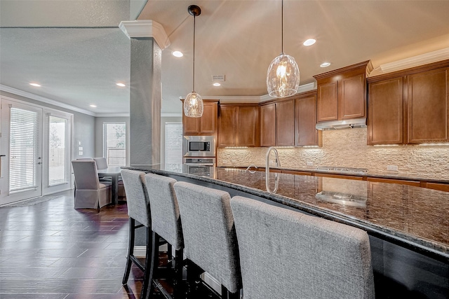 kitchen with appliances with stainless steel finishes, dark stone countertops, hanging light fixtures, tasteful backsplash, and ornamental molding