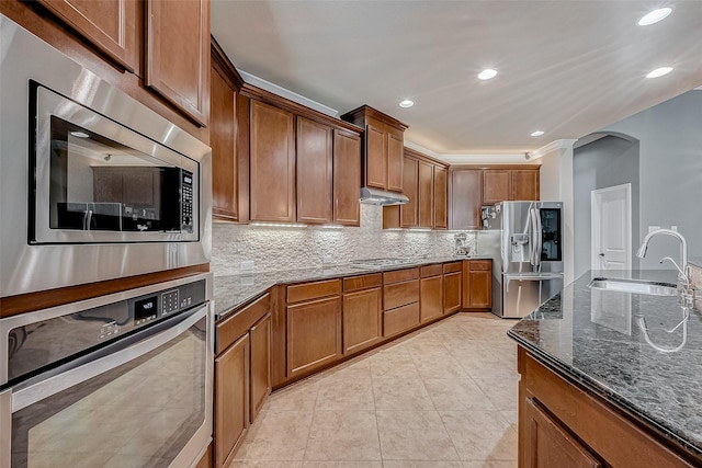 kitchen with appliances with stainless steel finishes, sink, dark stone countertops, and backsplash