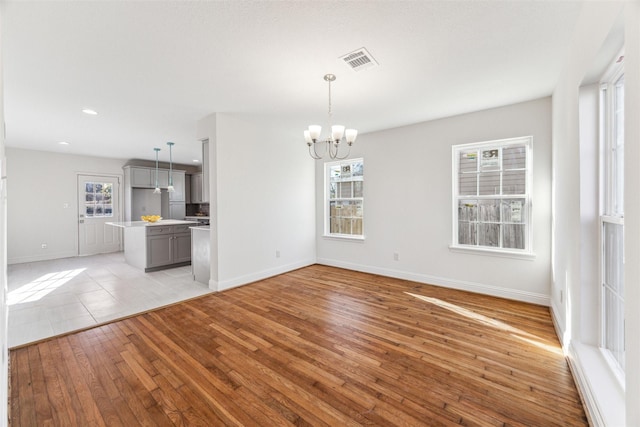 unfurnished living room with light wood-type flooring, an inviting chandelier, visible vents, and a wealth of natural light