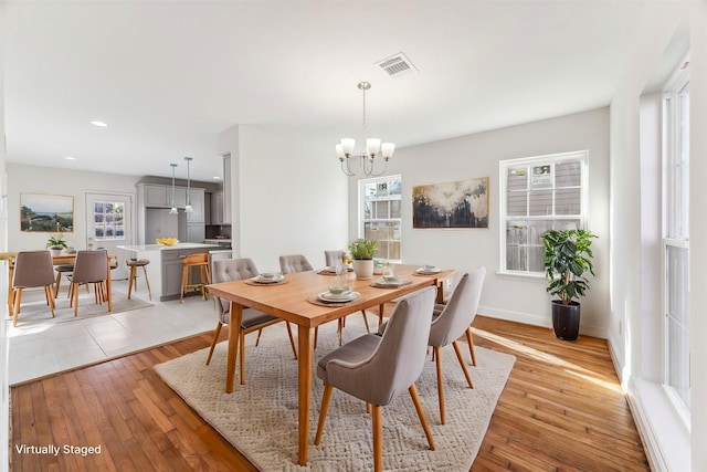 dining space featuring a chandelier, light wood-type flooring, a wealth of natural light, and visible vents