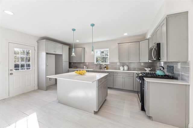 kitchen with gas range oven, stainless steel microwave, decorative backsplash, gray cabinetry, and a sink