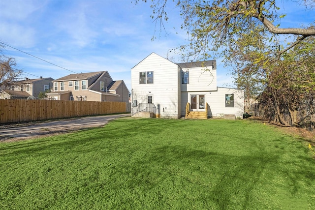 back of house featuring entry steps, a lawn, fence, and a residential view