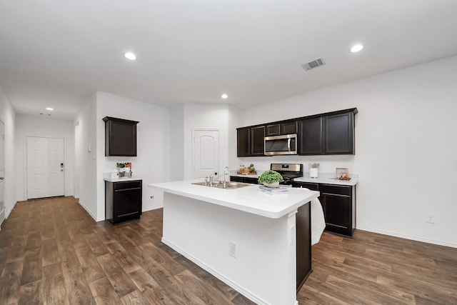 kitchen featuring dark wood-type flooring, appliances with stainless steel finishes, sink, and a kitchen island with sink