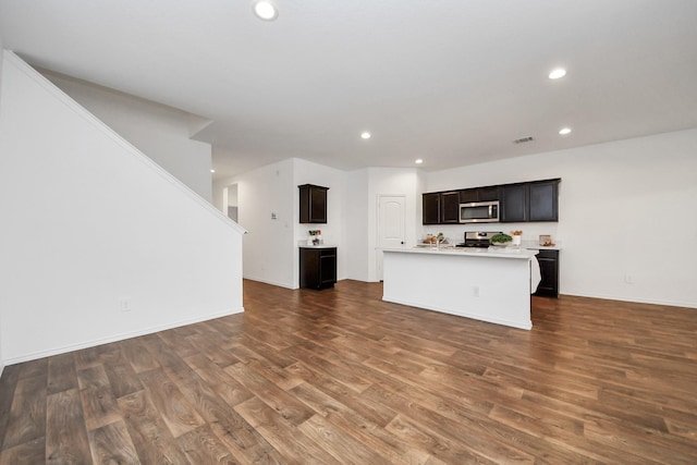 kitchen featuring dark brown cabinets, dark wood-type flooring, stainless steel appliances, and a center island with sink