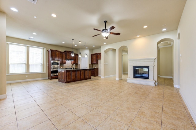 kitchen featuring light tile patterned floors, ceiling fan, a center island, stainless steel microwave, and decorative light fixtures