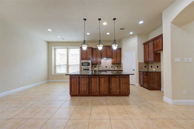 kitchen featuring tasteful backsplash, light tile patterned floors, appliances with stainless steel finishes, an island with sink, and pendant lighting