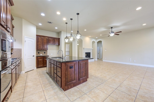 kitchen featuring sink, appliances with stainless steel finishes, a kitchen island with sink, hanging light fixtures, and decorative backsplash