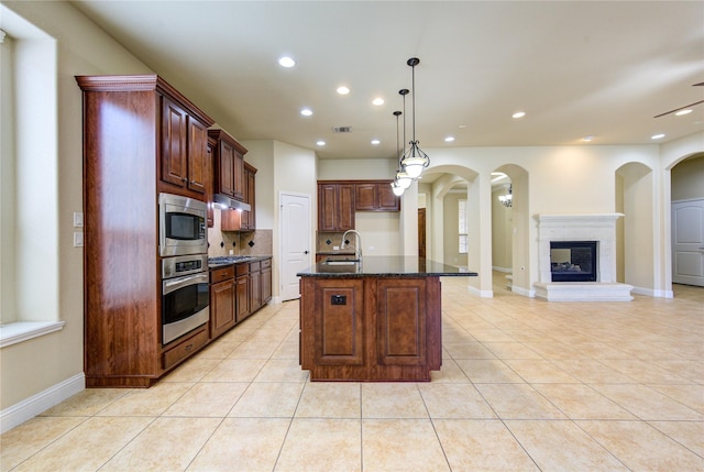 kitchen featuring light tile patterned floors, hanging light fixtures, stainless steel appliances, tasteful backsplash, and a center island with sink