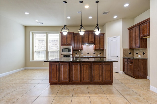 kitchen featuring a kitchen island with sink, hanging light fixtures, stainless steel appliances, and dark stone counters