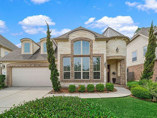 french provincial home with a garage, concrete driveway, brick siding, and stone siding