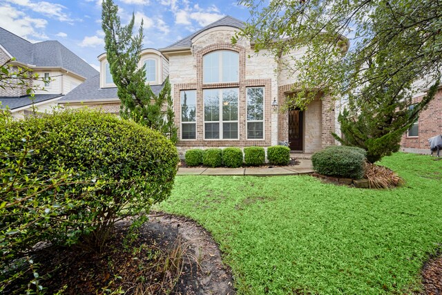 french provincial home featuring stone siding, a front lawn, and brick siding