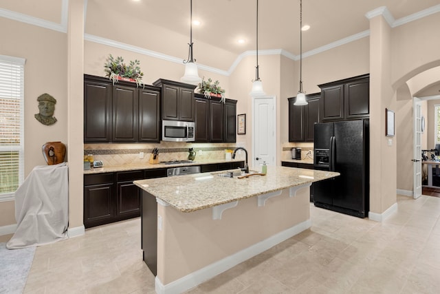 kitchen featuring a center island with sink, arched walkways, a breakfast bar area, stainless steel appliances, and a sink