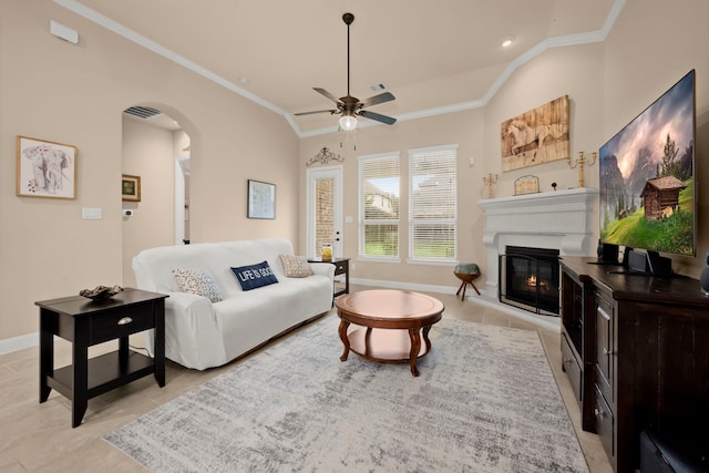 living room featuring arched walkways, lofted ceiling, ornamental molding, a glass covered fireplace, and baseboards