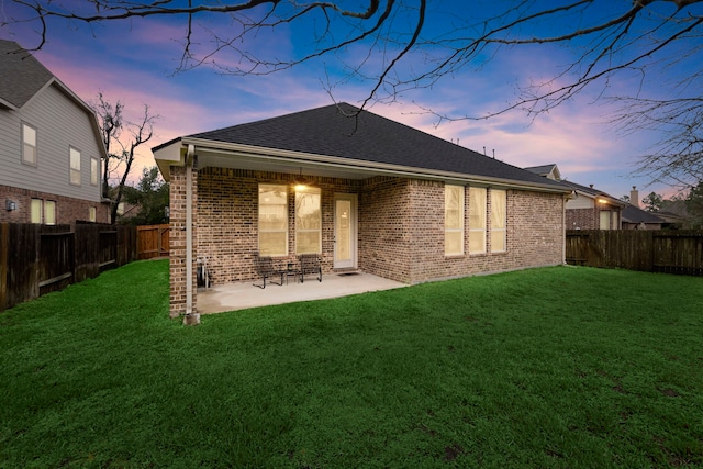 back of house at dusk featuring a patio area, brick siding, a lawn, and a fenced backyard