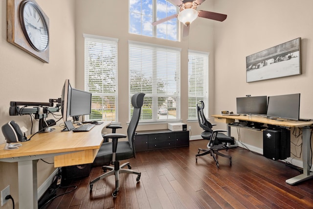 office featuring dark wood-style floors, a towering ceiling, baseboards, and a ceiling fan