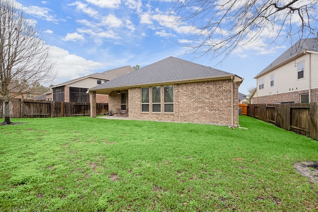 rear view of property with a shingled roof, a fenced backyard, a yard, a patio area, and brick siding