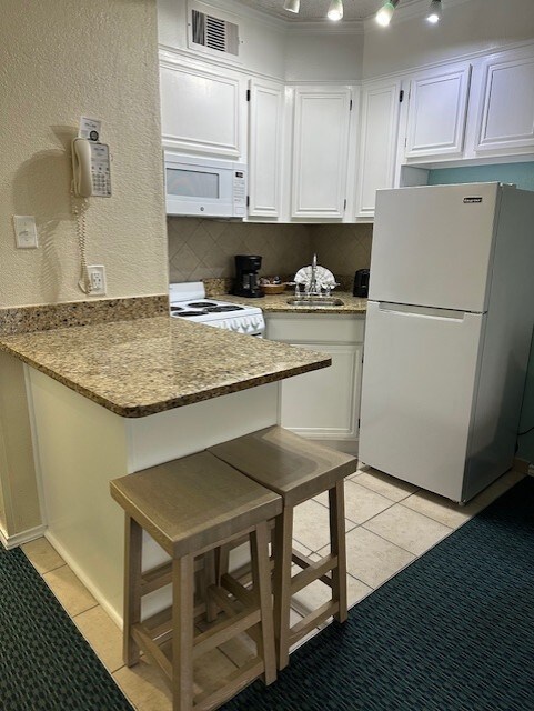 6102 Seawall Blvd Unit 128, Galveston, TX 77551 - kitchen featuring light tile patterned floors, white appliances, visible vents, white cabinets, and backsplash