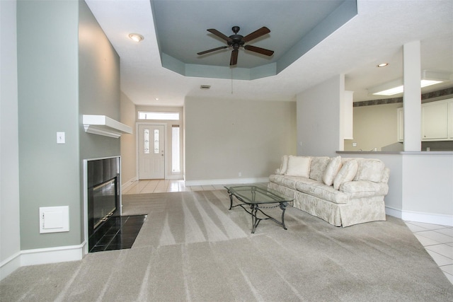 unfurnished living room featuring a raised ceiling, a premium fireplace, light tile patterned floors, and ceiling fan