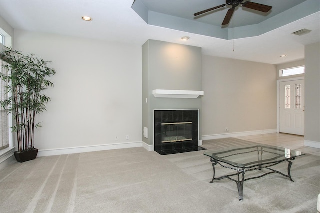 carpeted living room featuring a tray ceiling, a fireplace, and ceiling fan