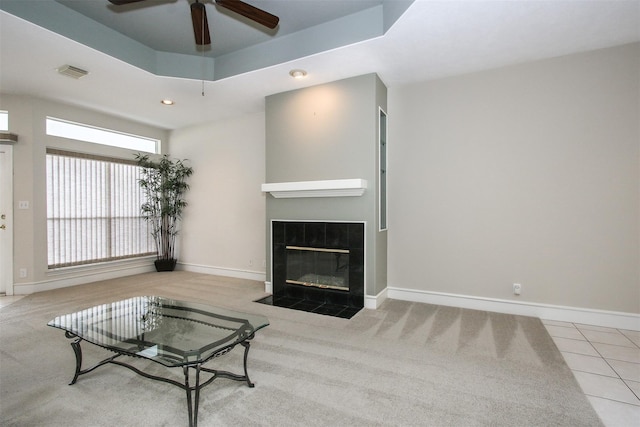 living room featuring a raised ceiling, a tiled fireplace, tile patterned flooring, and ceiling fan