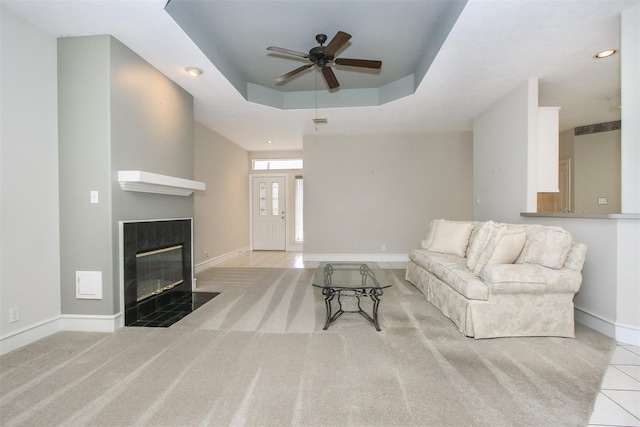 carpeted living room with a premium fireplace, a raised ceiling, and ceiling fan