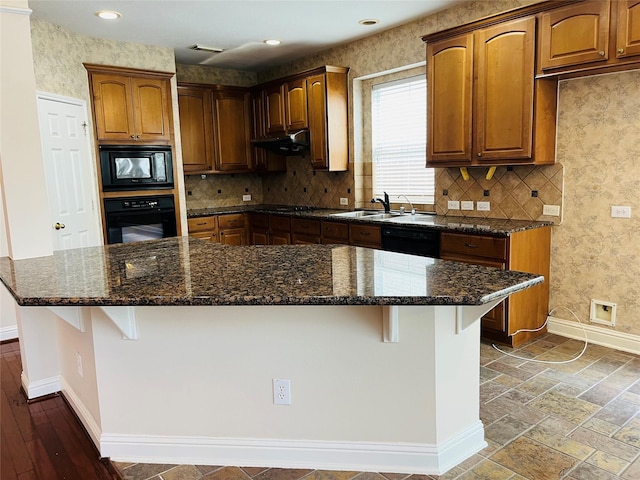 kitchen with sink, a breakfast bar area, dark stone countertops, a center island, and black appliances