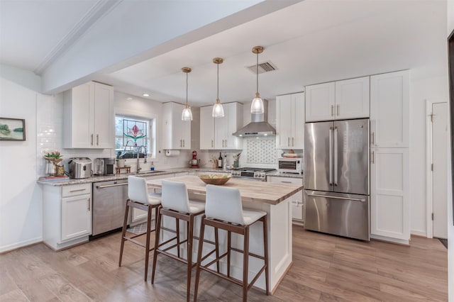 kitchen with stainless steel appliances, butcher block counters, a sink, visible vents, and wall chimney range hood