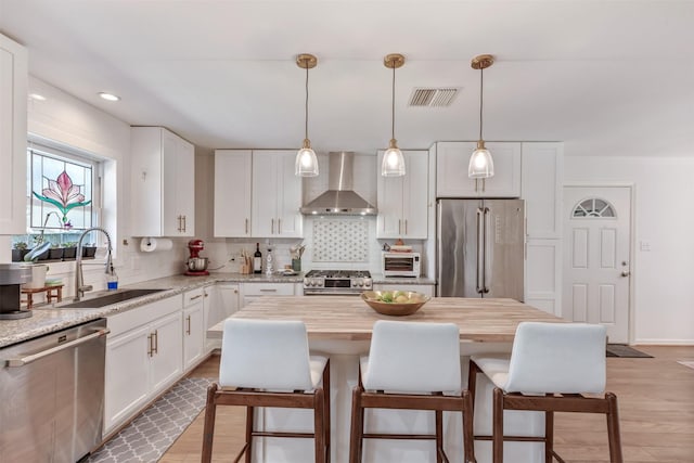 kitchen featuring a breakfast bar area, stainless steel appliances, visible vents, a sink, and wall chimney exhaust hood