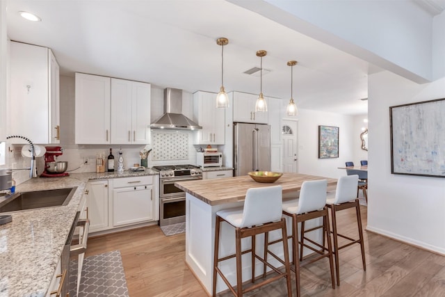 kitchen with stainless steel appliances, butcher block counters, a sink, wall chimney range hood, and tasteful backsplash