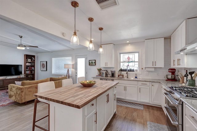 kitchen with range with two ovens, butcher block countertops, a sink, visible vents, and open floor plan