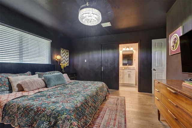 bedroom featuring a chandelier, ensuite bath, and light wood-style flooring