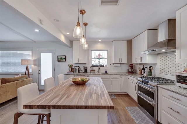 kitchen with butcher block counters, visible vents, decorative backsplash, double oven range, and wall chimney exhaust hood