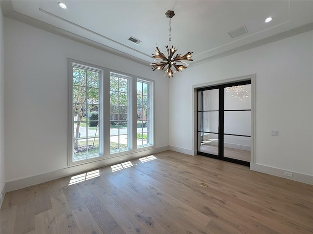 unfurnished room with a raised ceiling, a chandelier, and light wood-type flooring