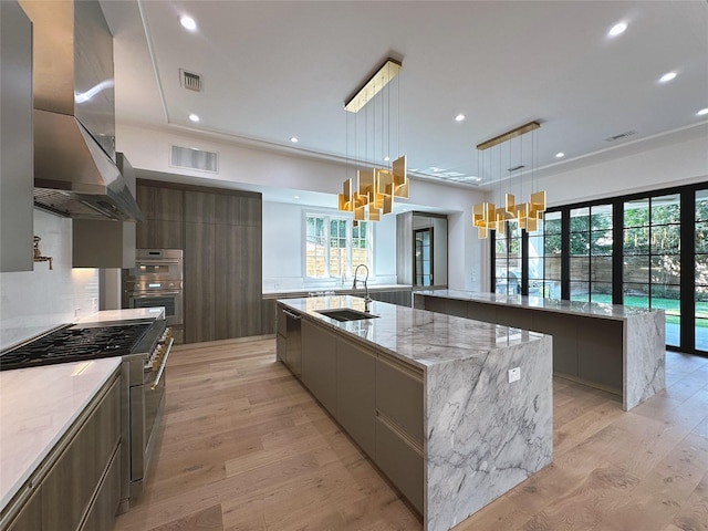 kitchen with extractor fan, sink, hanging light fixtures, and a large island with sink