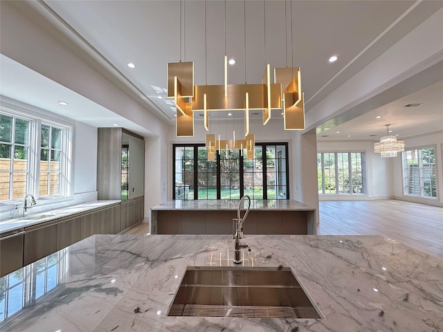 kitchen featuring light stone counters, decorative light fixtures, sink, and light wood-type flooring