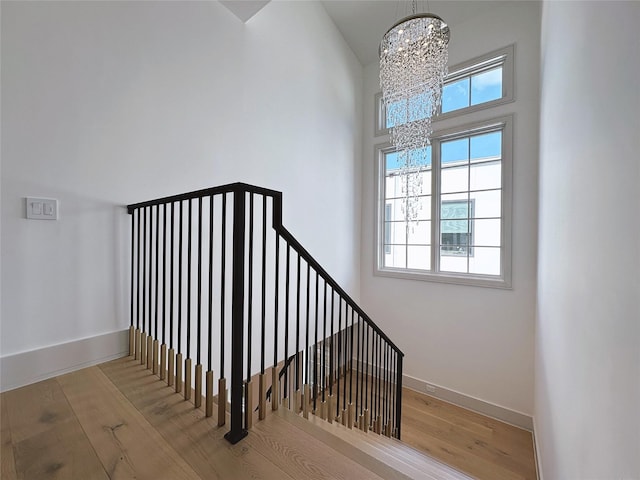 stairway featuring a towering ceiling, wood-type flooring, and a chandelier