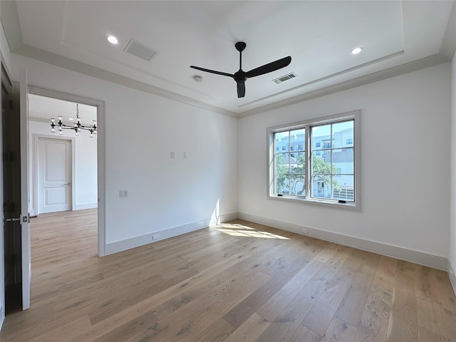 unfurnished room with ornamental molding, a tray ceiling, ceiling fan with notable chandelier, and light hardwood / wood-style flooring