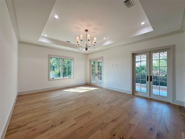 unfurnished room with a notable chandelier, a tray ceiling, french doors, and light wood-type flooring