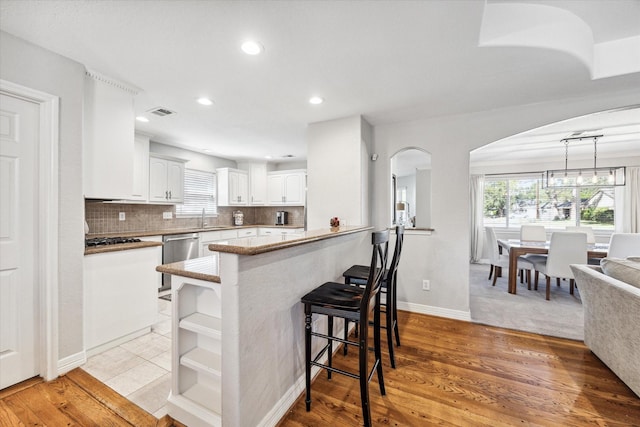 kitchen featuring sink, tasteful backsplash, white cabinets, stainless steel dishwasher, and kitchen peninsula