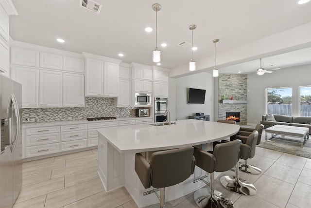 kitchen featuring white cabinetry, hanging light fixtures, backsplash, stainless steel appliances, and an island with sink