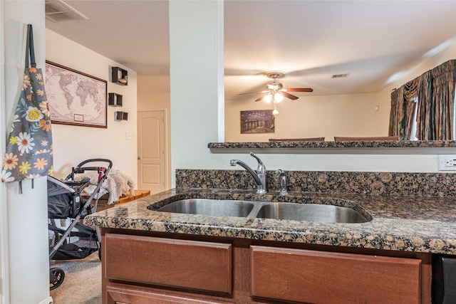 kitchen featuring sink, dark stone countertops, ceiling fan, and carpet flooring